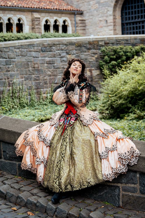 Andrea as Christine Daae in the Aminta costume from Point of No Return, seated on a stone wall in Fort Tryon Park