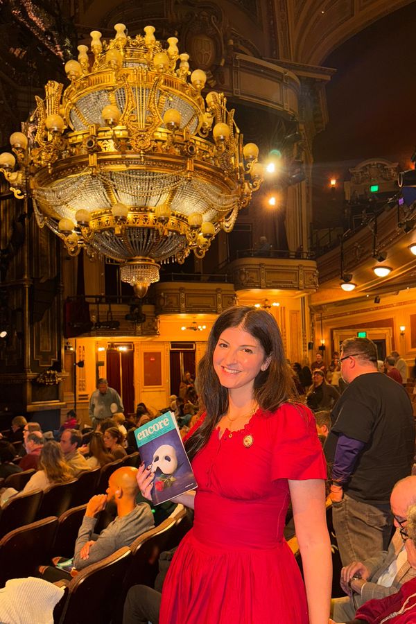 Andrea in a red dress at the theater holding a Phantom of the Opera Playbill