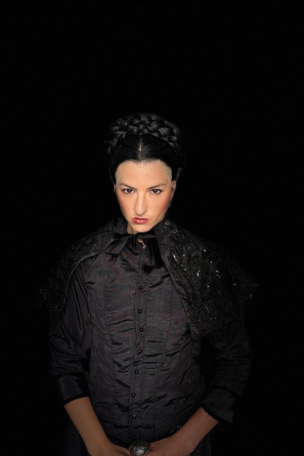 Andrea as Madame Giry in a black jacket and capelet with a braided wig